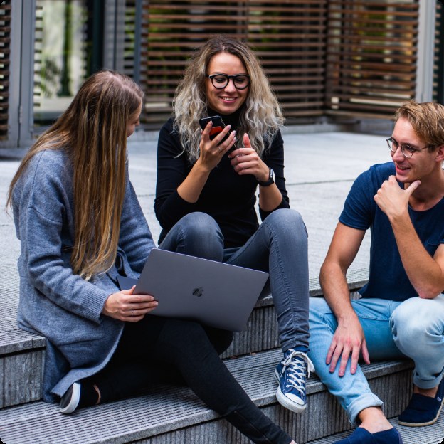 Tre unge sidder sammen udenfor med telefon og bærbar